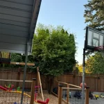 A backyard featuring a basketball hoop and a swing set, providing space for outdoor play and recreation.