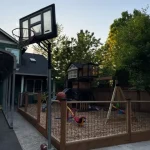 A basketball hoop with a net stands on a driveway, ready for play under clear blue skies.