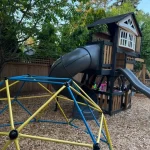 A playground featuring a colorful slide and a swing set, surrounded by grass and trees.