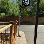 A basketball hoop with a net stands on a driveway, ready for play under clear blue skies.