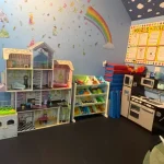 A colorful room filled with various toys and dolls scattered across the floor, creating a playful atmosphere.