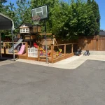 A backyard featuring a basketball court, swings, and a swing set, providing a space for outdoor recreation and play.