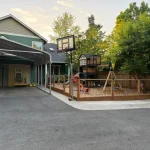 A backyard featuring a basketball court, swings, and a swing set, providing a space for outdoor recreation and play.